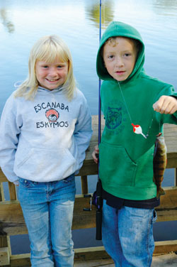 Two young children standing on fishing pier holding fishing rod and bobber.